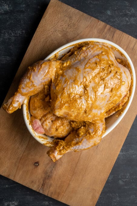 Whole chicken coated with spiced butter marinade in a white oval pan.