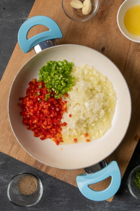 Finely chopped red and green peppers and onion in a white pan.