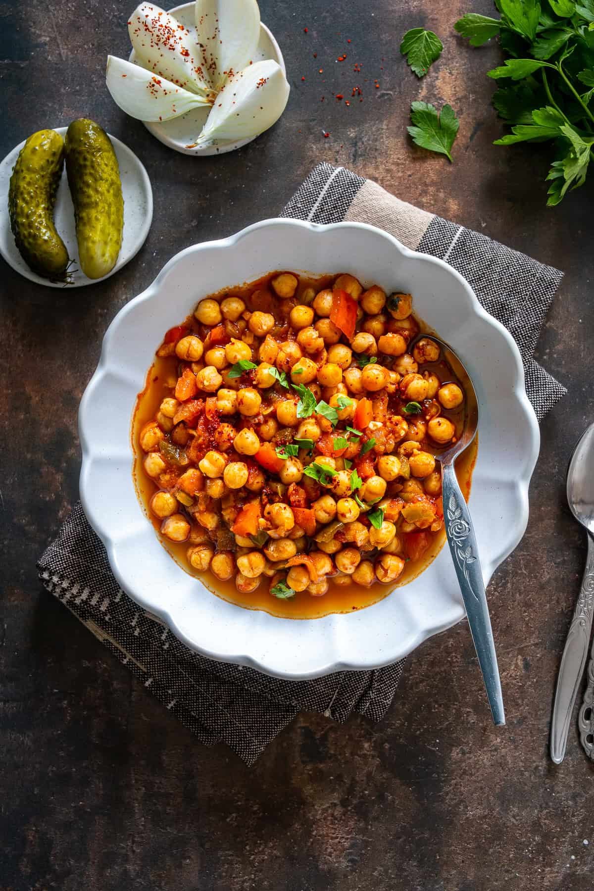 Turkish chickpea stew (Etsiz Nohut Yemeği) served in a white bowl, garnished with parsley, with pickles and onion slices on the side.