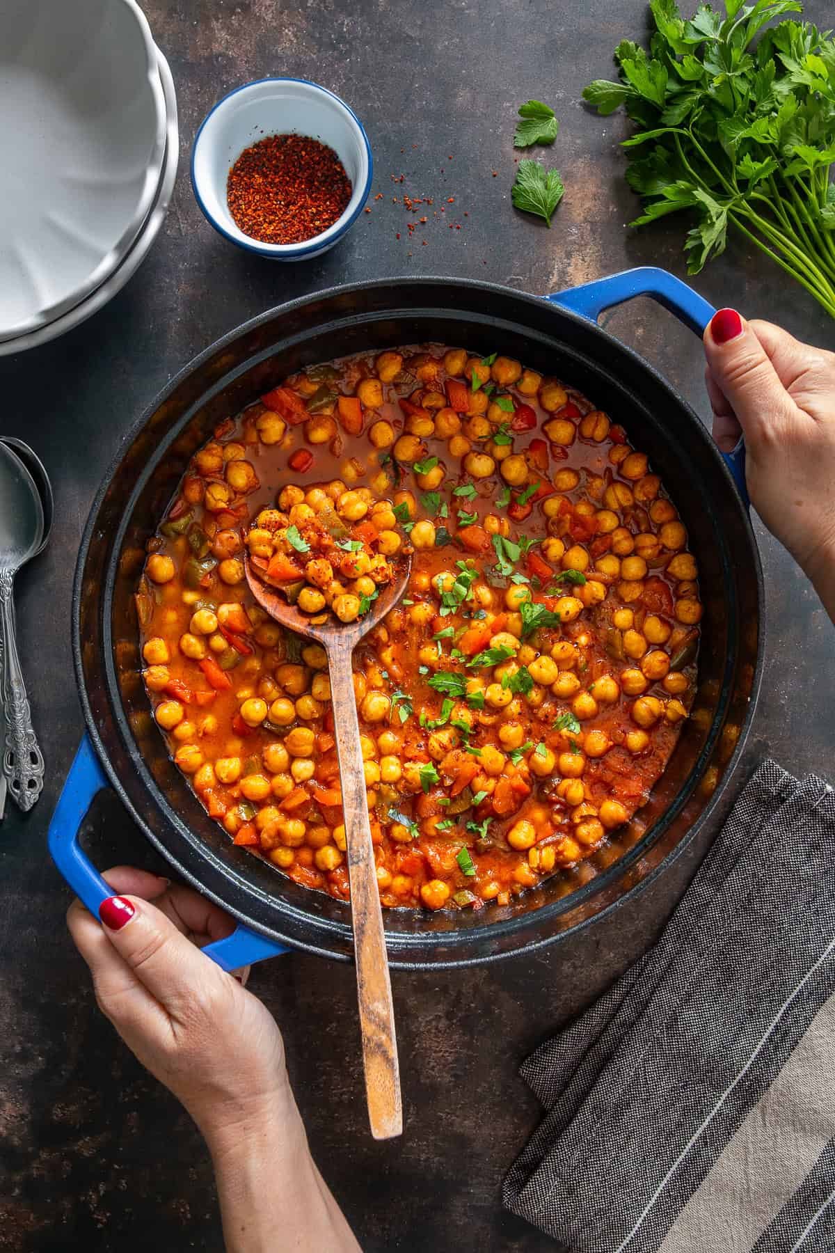 Turkish chickpea stew (Etsiz Nohut Yemeği) in a blue pot, garnished with parsley and stirred with a wooden spoon.