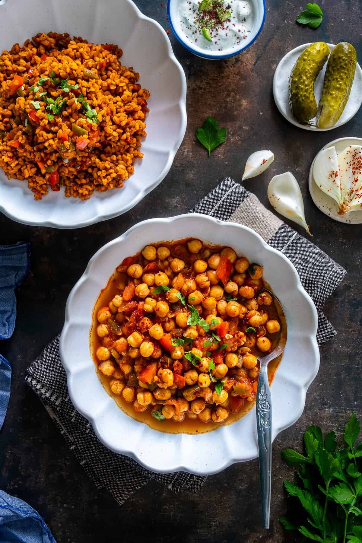 Turkish chickpea stew (Etsiz Nohut Yemeği) served with bulgur pilaf, cacik, pickles, and onion on the side.