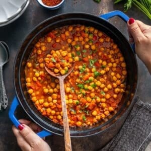 Turkish chickpea stew (Etsiz Nohut Yemeği) simmering in a blue pot, garnished with parsley and stirred with a wooden spoon.