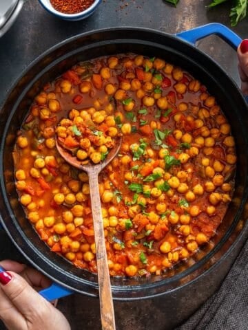 Turkish chickpea stew (Etsiz Nohut Yemeği) simmering in a blue pot, garnished with parsley and stirred with a wooden spoon.