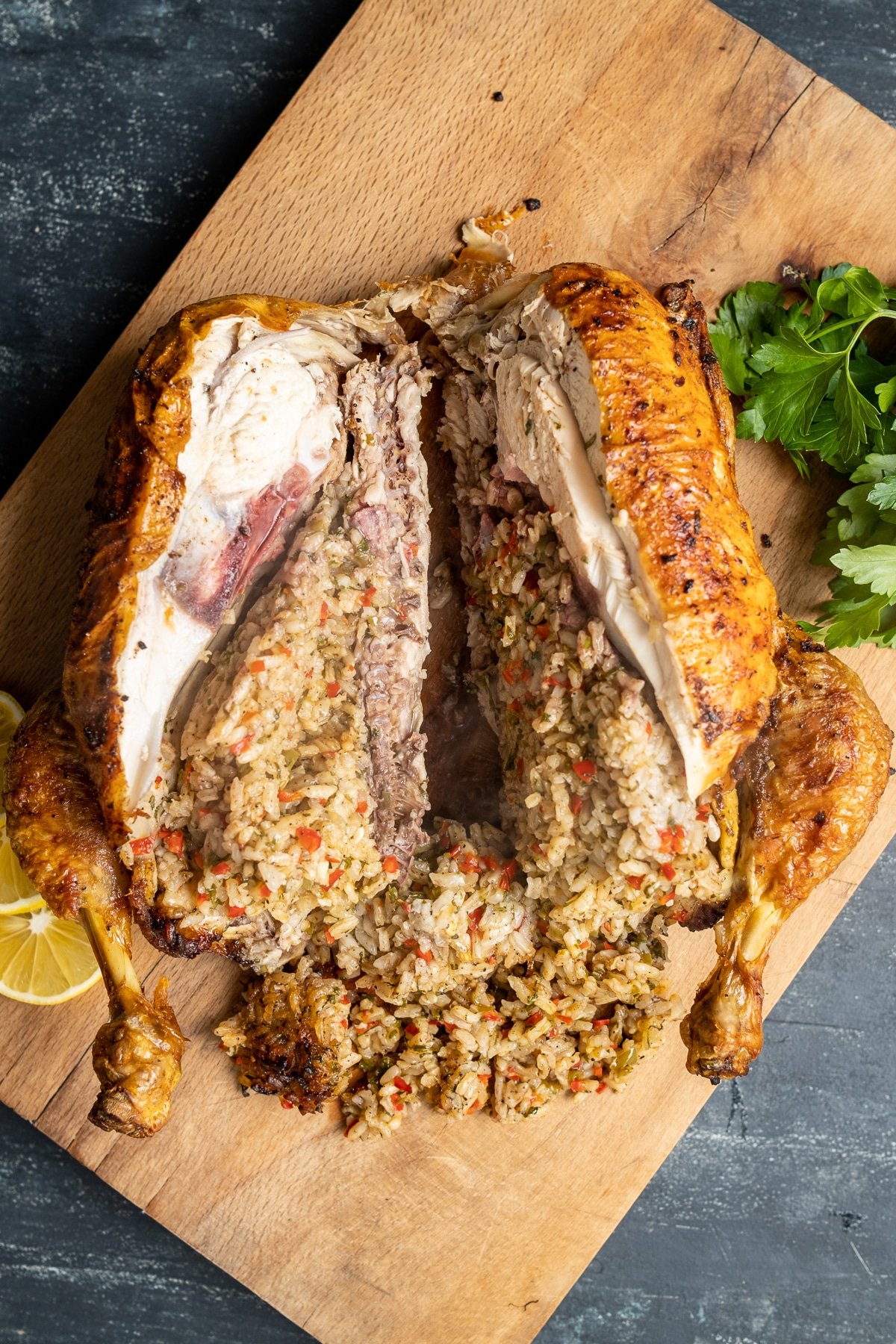 Roasted rice stuffed whole chicken is cut in the middle on a wooden board.