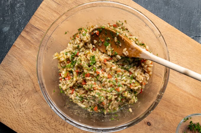 Rice stuffing with spices and herbs in a glass bowl, a wooden spoon inside it.