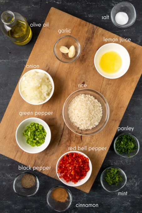 Rice, garlic, chopped red and green bell peppers, herbs, spices on a wooden board and on a dark background.