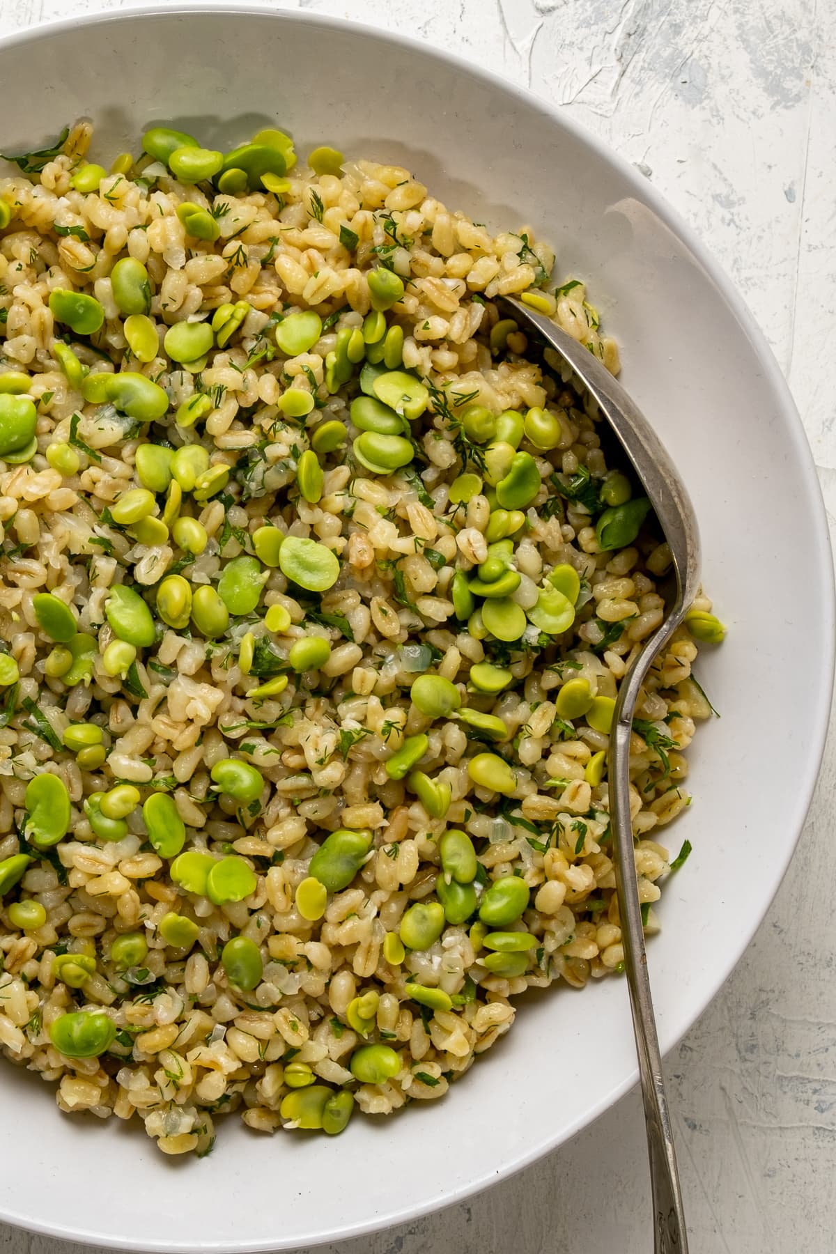 Bulgur pilaf with fava beans in a white bowl and a spoon inside it.