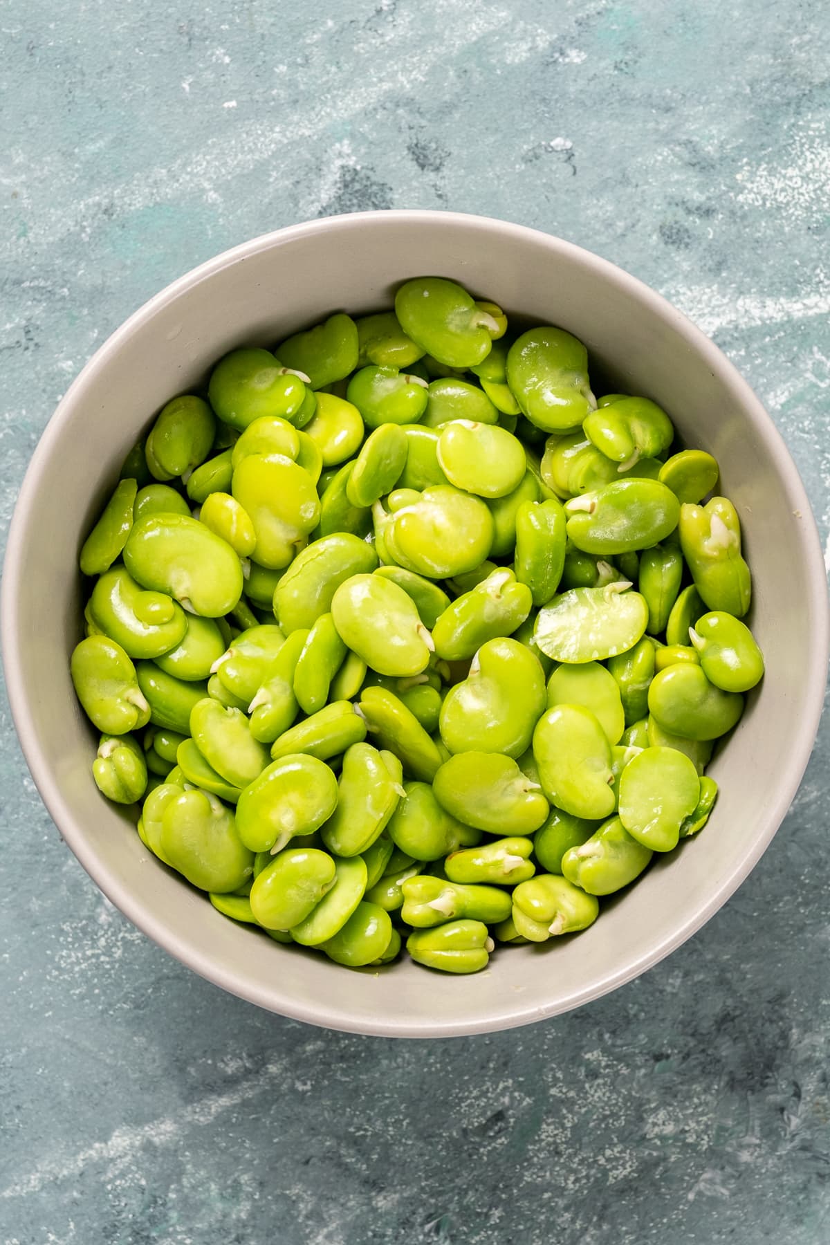 Bright green color shelled fresh fava beans in a white bowl.