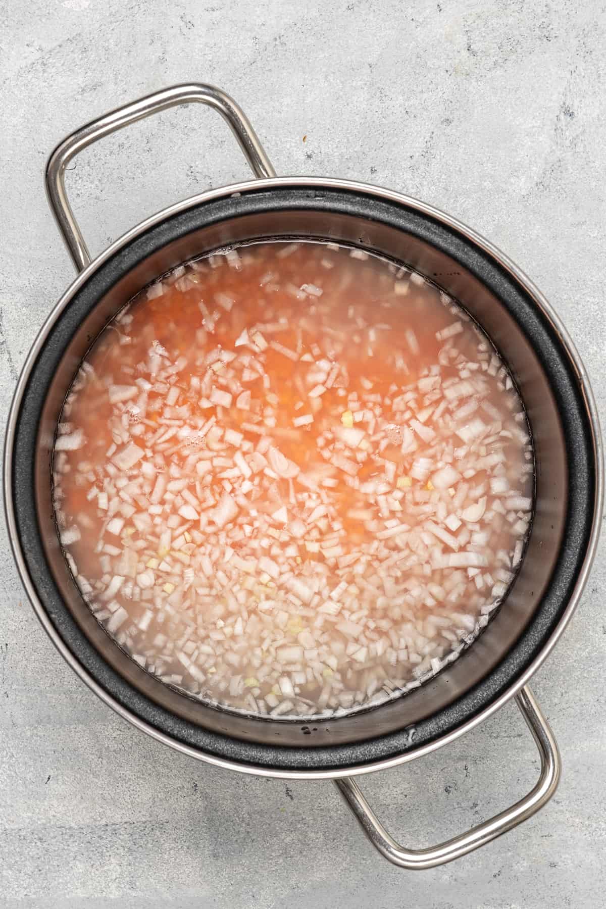 Red lentils and chopped onions in a pot with water.