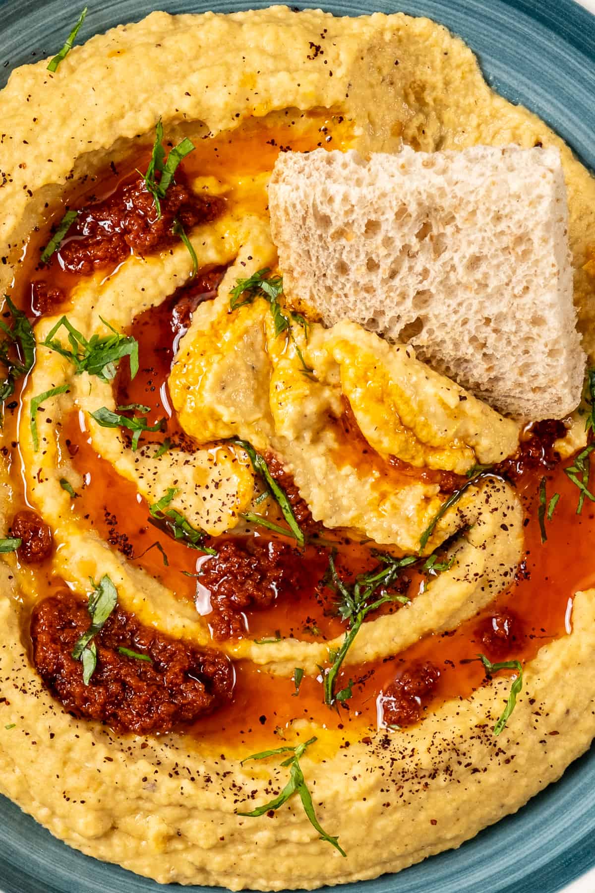 Close shot of lentil hummus with tomato paste oil sauce and a piece of bread in it.