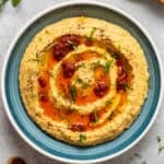 Lentil hummus topped with tomato paste oil sauce and minced parsley in a blue bowl.