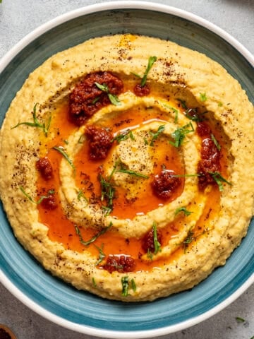 Lentil hummus topped with tomato paste oil sauce and minced parsley in a blue bowl.