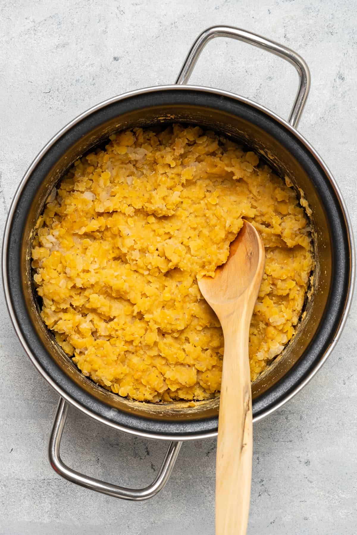 Cooked red lentils in a pot and a wooden spoon inside it.