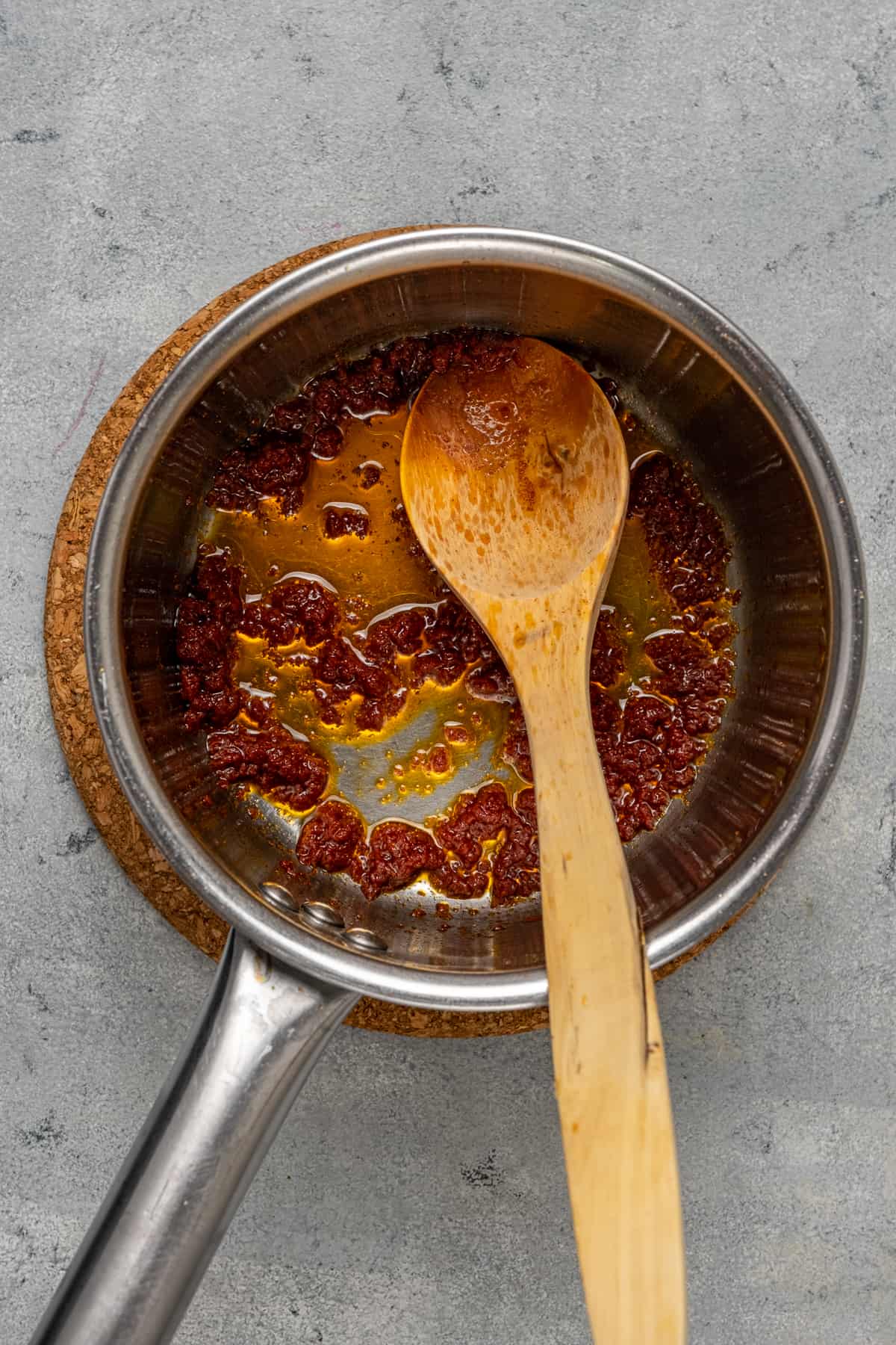 Tomato paste oil sauce in a small saucepan and a wooden spoon inside it.