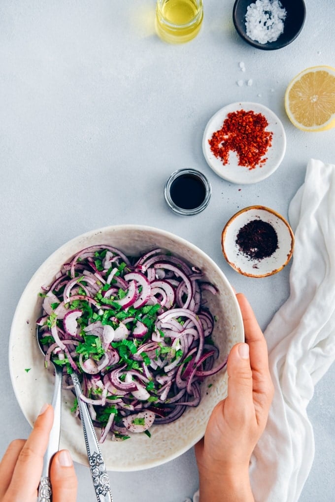 Would you like to take your picnic food to next level?Serve it with sumac onions! #sumac #turkishfood #onionsalad #onionrecipe Hands serving sumac onions in a white bowl
