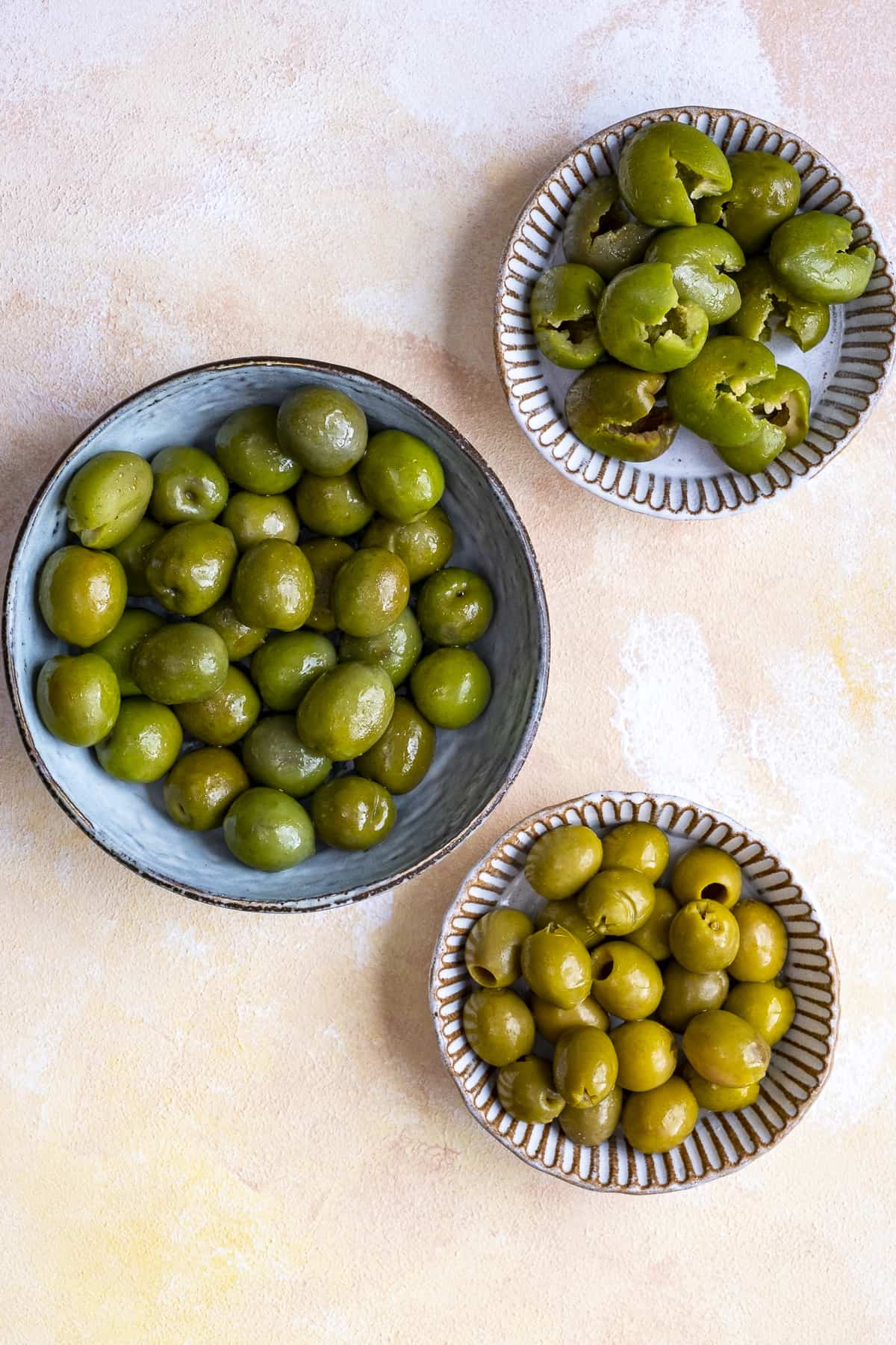 Whole green olives and pitted green olives in three bowls.