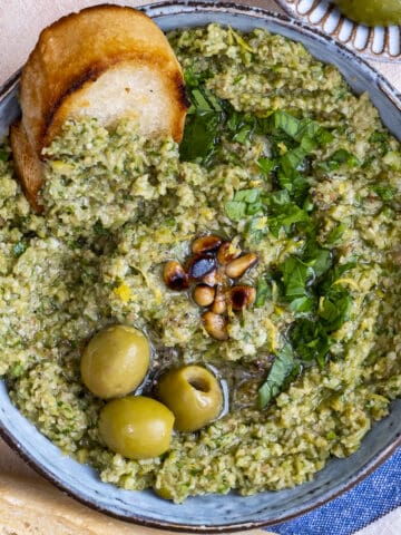 Green olive tapenade topped with pine nuts and olives, a crostini in it.