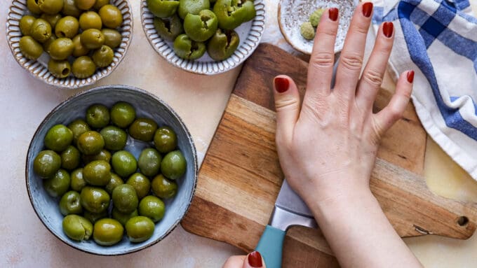 Hands showing how to pit green olives with a knife.