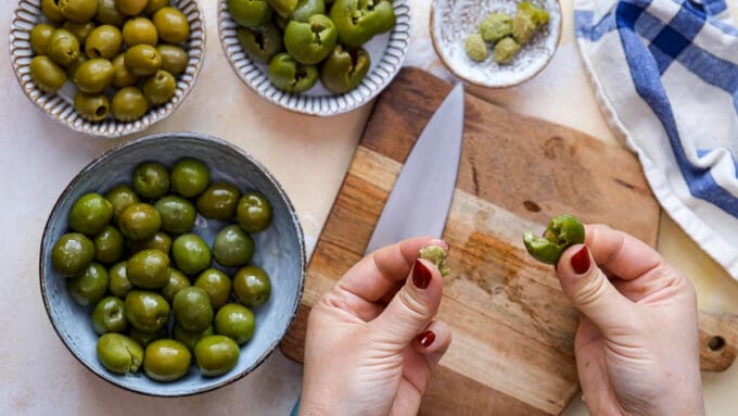 Hands removing pit from green olives.