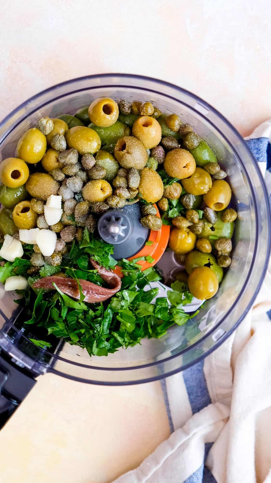 Green olives, parsley, capers, garlic, anchovy fillet in a food processor bowl.