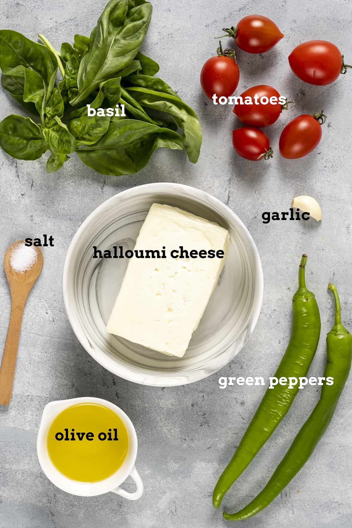 A block of halloumi cheese, olive oil, green peppers, cherry tomatoes, basil and garlic on a grey background.