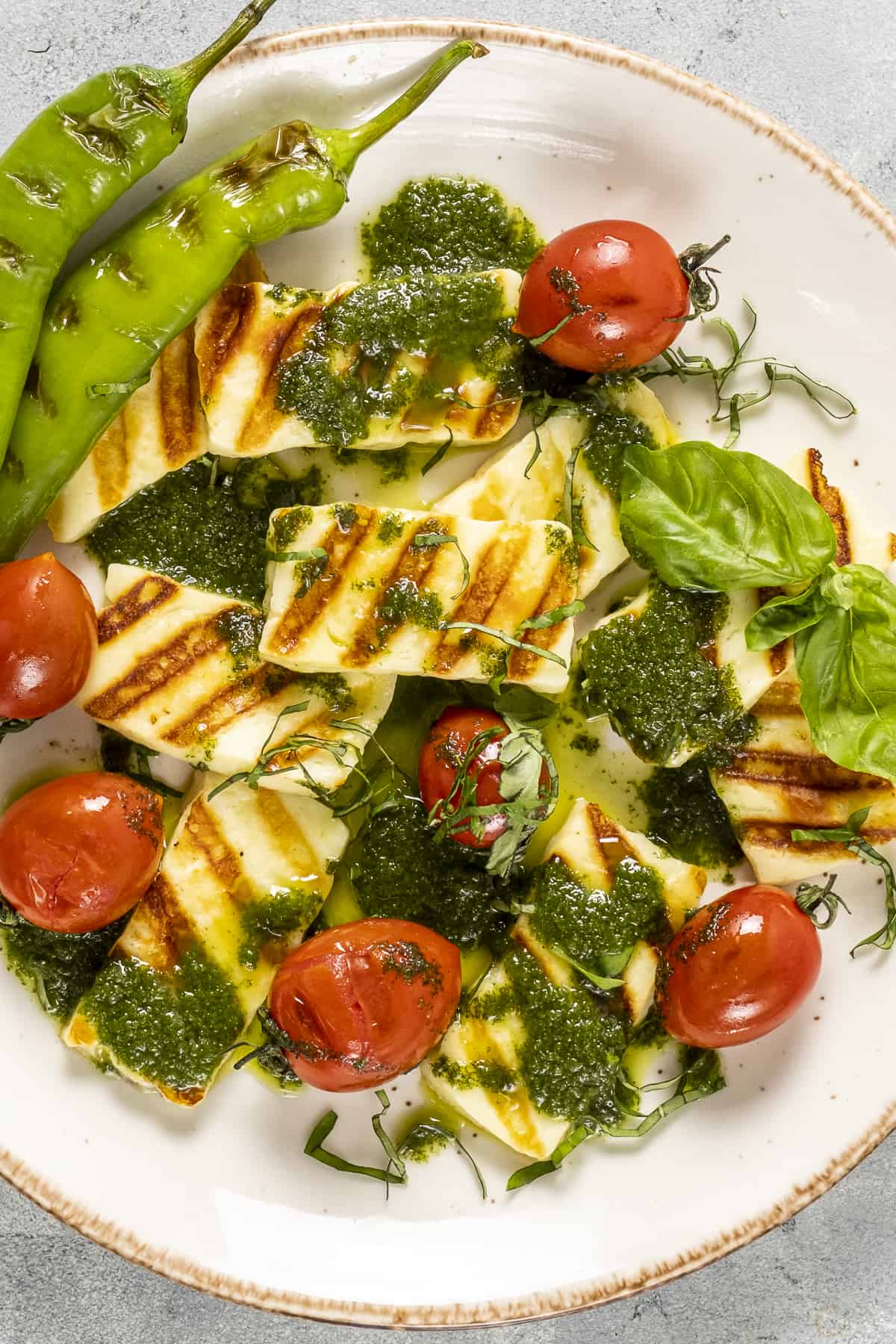 Grilled halloumi cheese with tomatoes and peppers on a white plate.