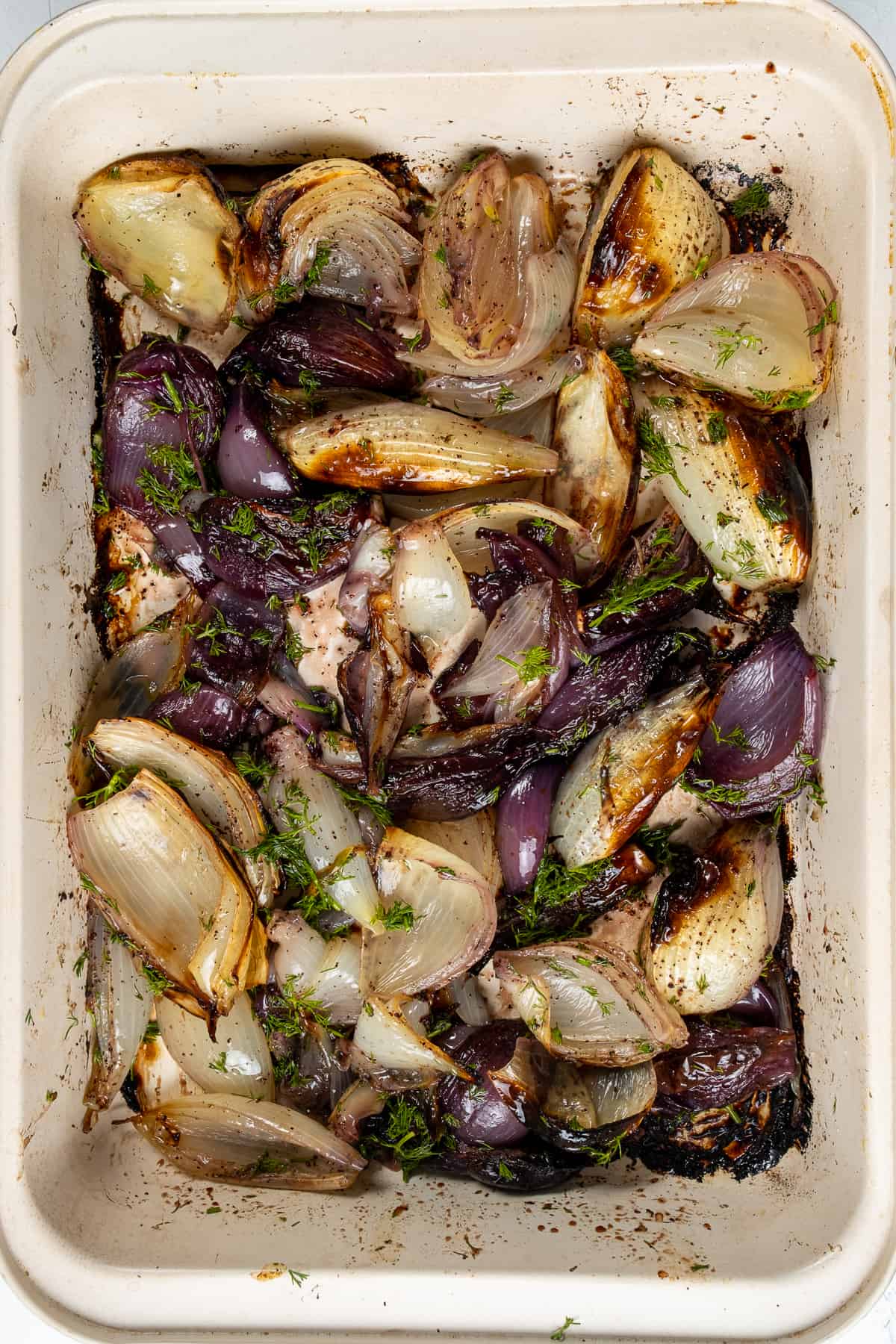 Baked red and white onion wedges combined with fresh dill, sumac, olive oil and pomegranate molasses in a white baking dish.