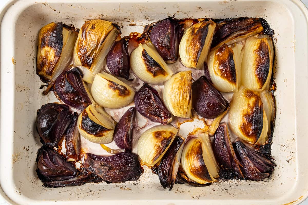 Roasted red and yellow onions in a white baking dish.