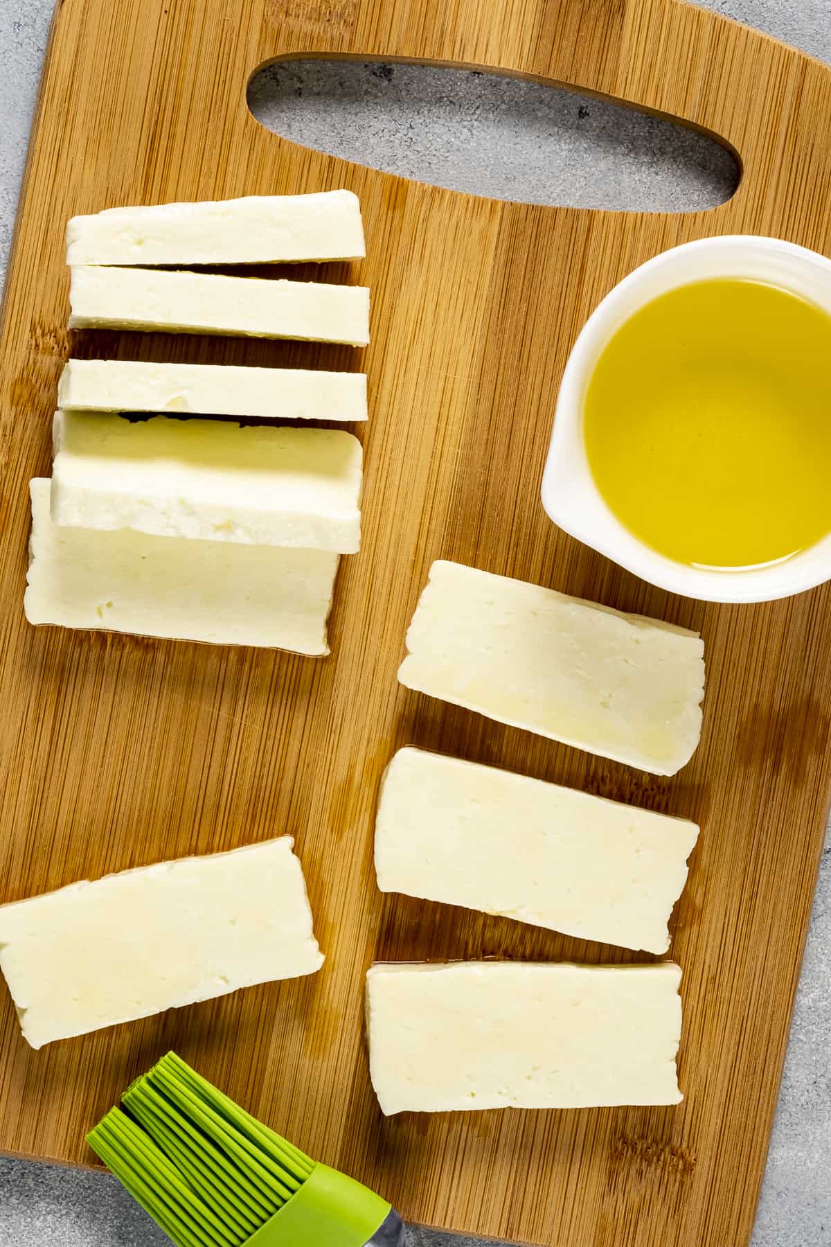 Halloumi slices on a wooden board and olive oil in a small bowl on the side.