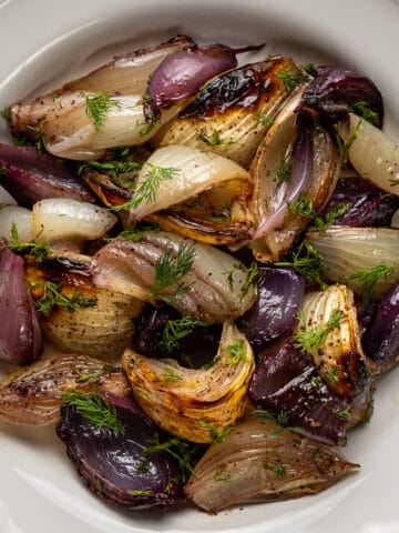 Red onions and yellow onions are roasted and combined with fresh dill and pomegranate molasses in a white bowl.