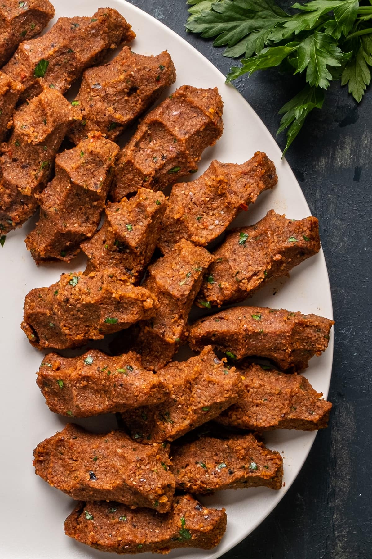 Turkish vegan cig kofte with bulgur and spices as a finger food on a white plate.