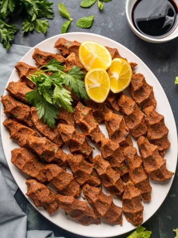 vegan cig kofte on a white oval plate, garnished with lemon wedges and parsley.