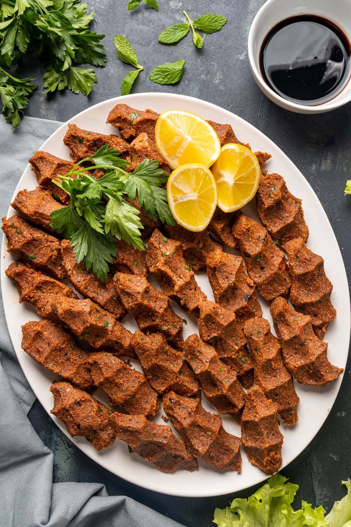 vegan cig kofte on a white oval plate, garnished with lemon wedges and parsley.