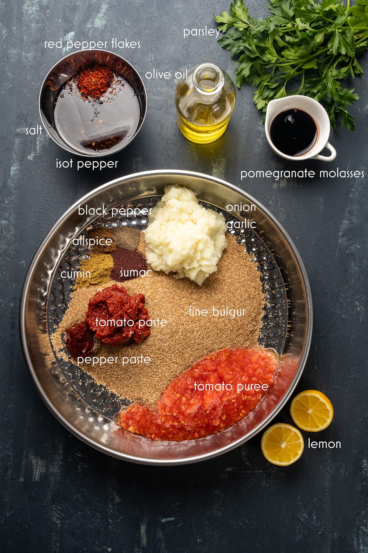 Fine bulgur, spices, pureed onion and garlic, pureed tomato, pepper and tomato paste in a traditional tray and pomegranate molasses, a mixture of olive oil, red pepper flakes and isot pepper in another bowl on the side.