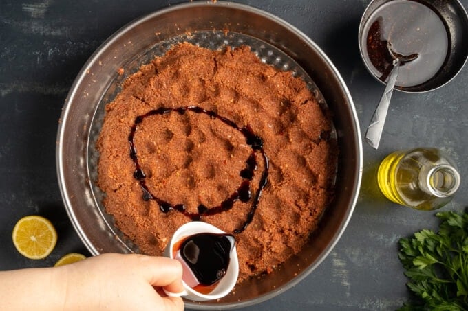 A hand drizzling pomegranate molasses over a fine bulgur mixture to make cigkofte.