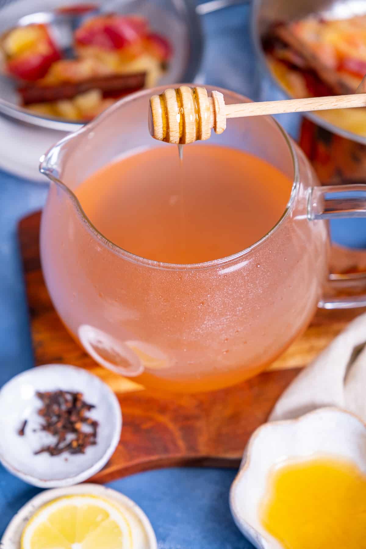 Honey is being added into the apple tea in a glass teapot.