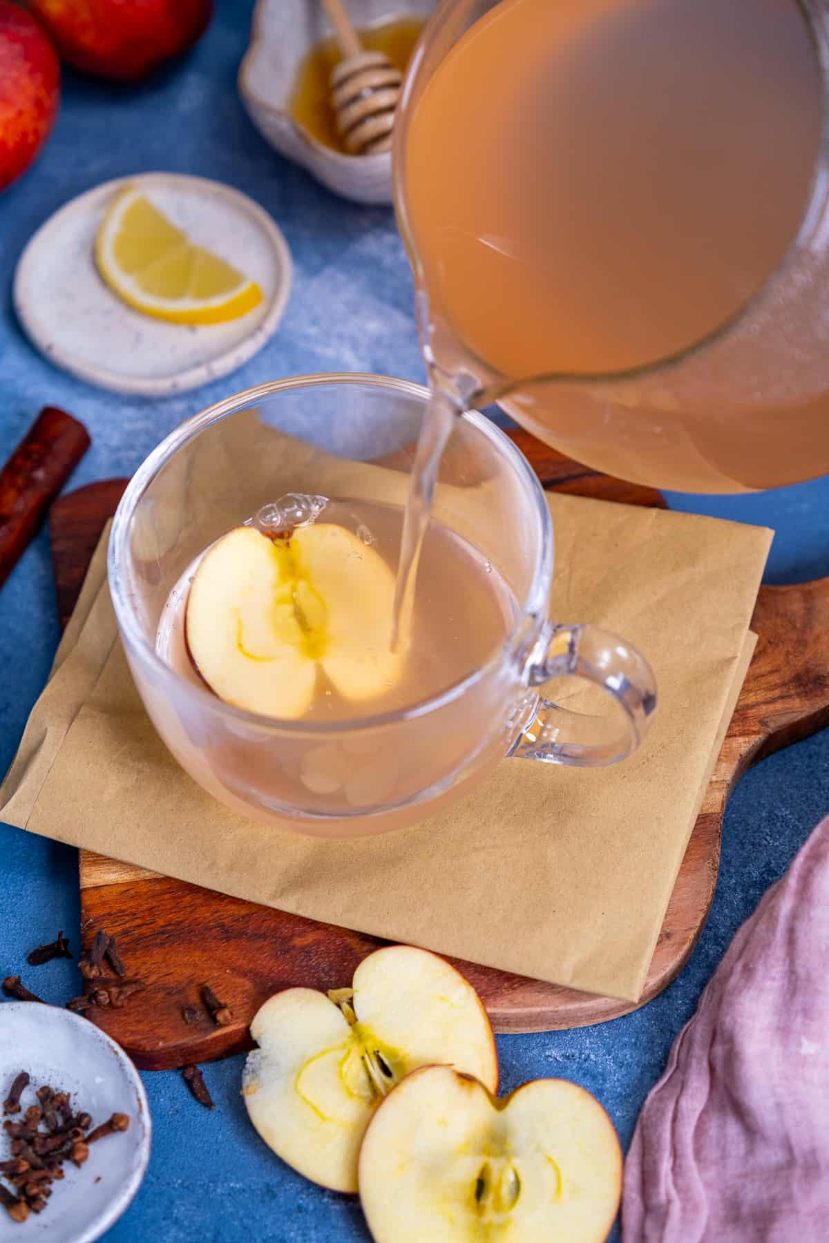 Apple tea is being poured into a glass cup from a glass teapot.