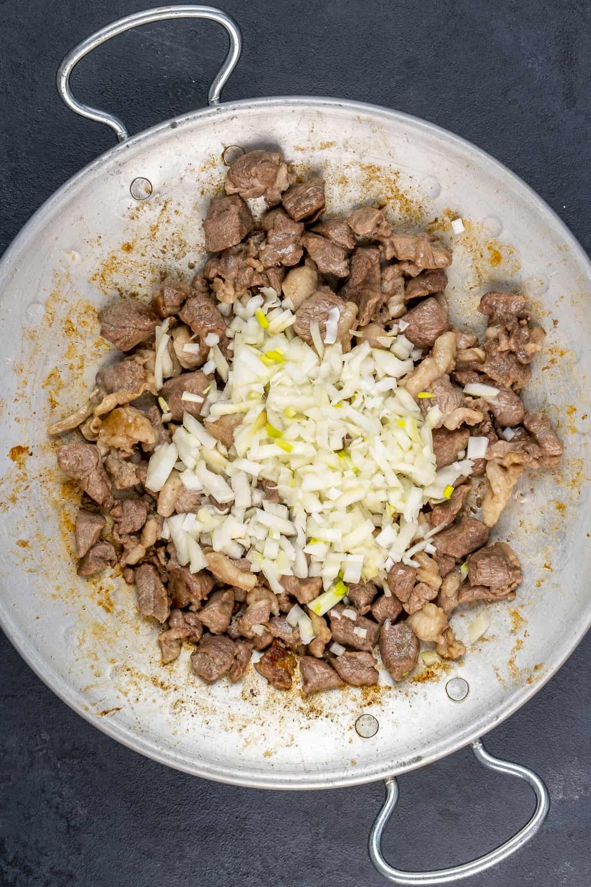 Chopped onion is added on the diced lamb cooking in a traditional pan.