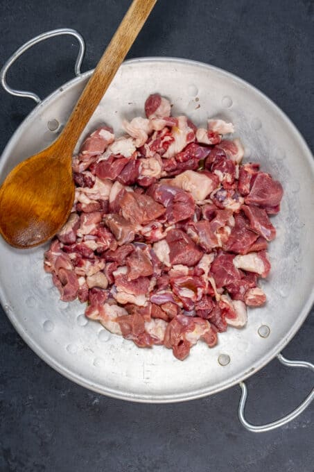 Uncooked diced lamb meat in a traditional pan.