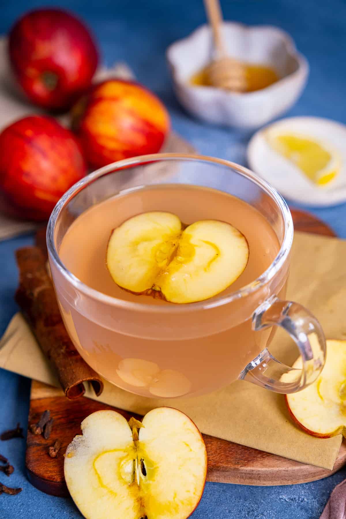 Apple tea in a glass mug, apples, lemon slice and honey behind it.