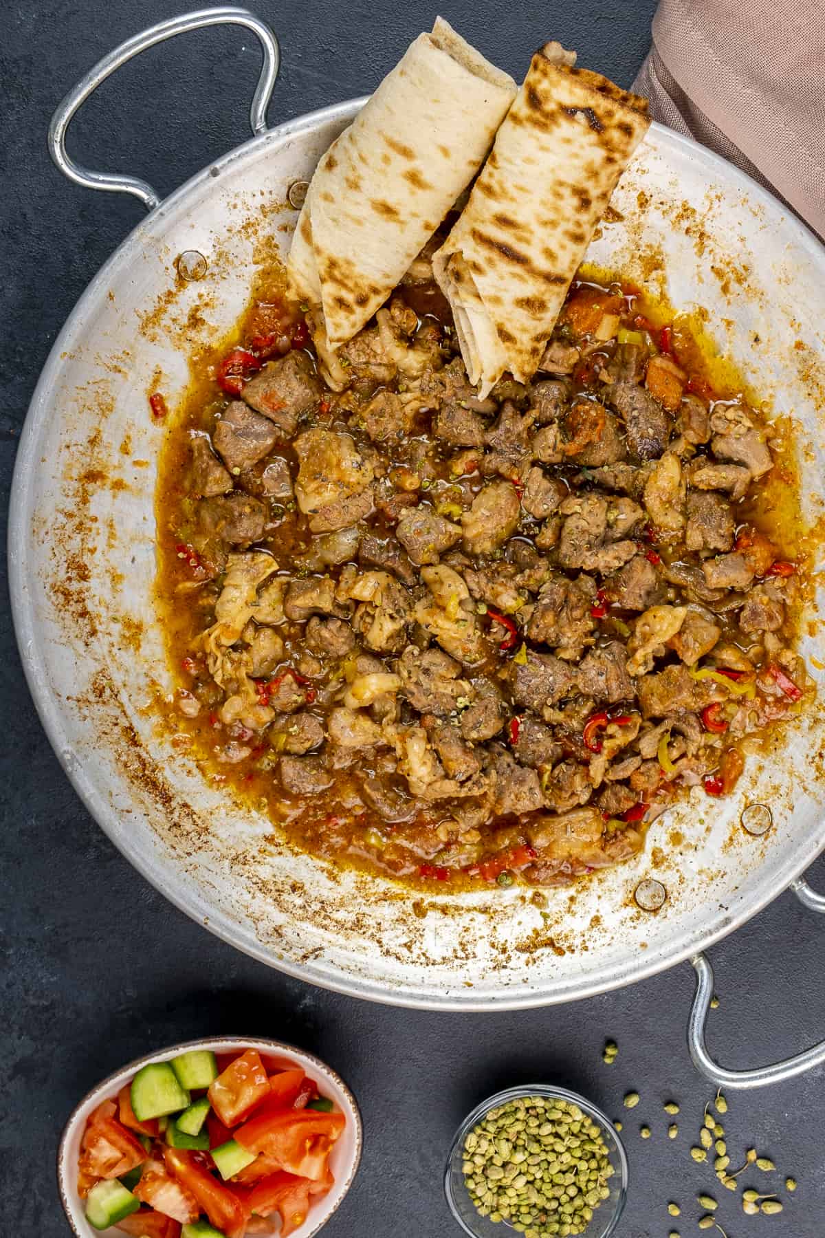 Diced lamb cooked in a pan, rolls of lavash bread are placed on the side.