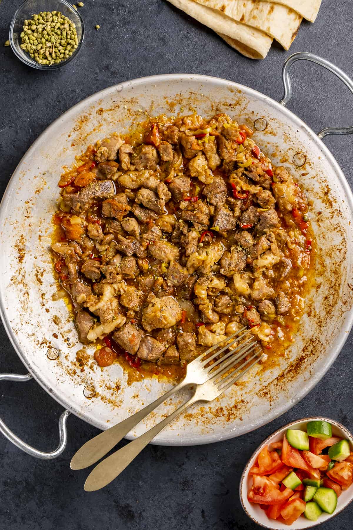 Sac kavurma in a traditional pan and lavash bread, diced tomatoes and cucumbers and oregano on the side.