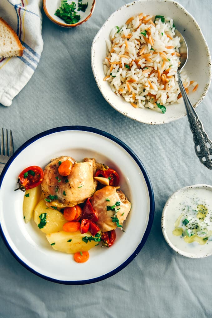 Roast chicken with vegetables in a white bowl accompanied by yogurt dip and rice