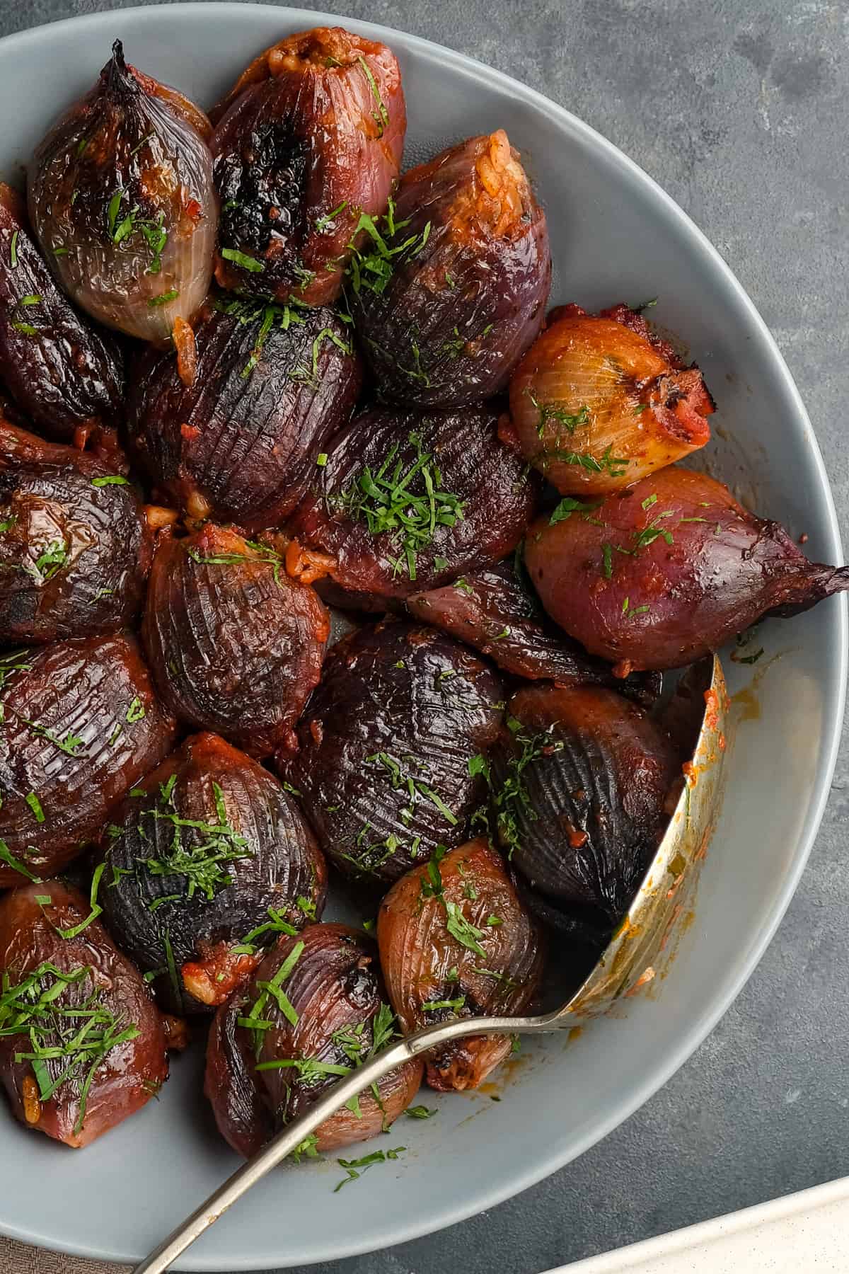 Baked stuffed onions in tomato sauce garnished with shopped parsley in a white dish with a spoon inside it.