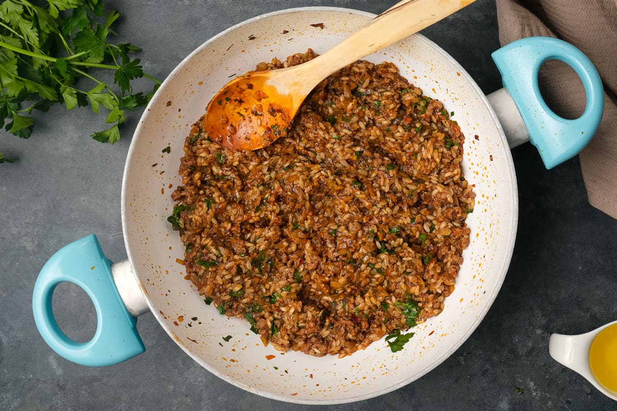 Spicy ground beef and rice filling in a white pan and a wooden spoon inside it.