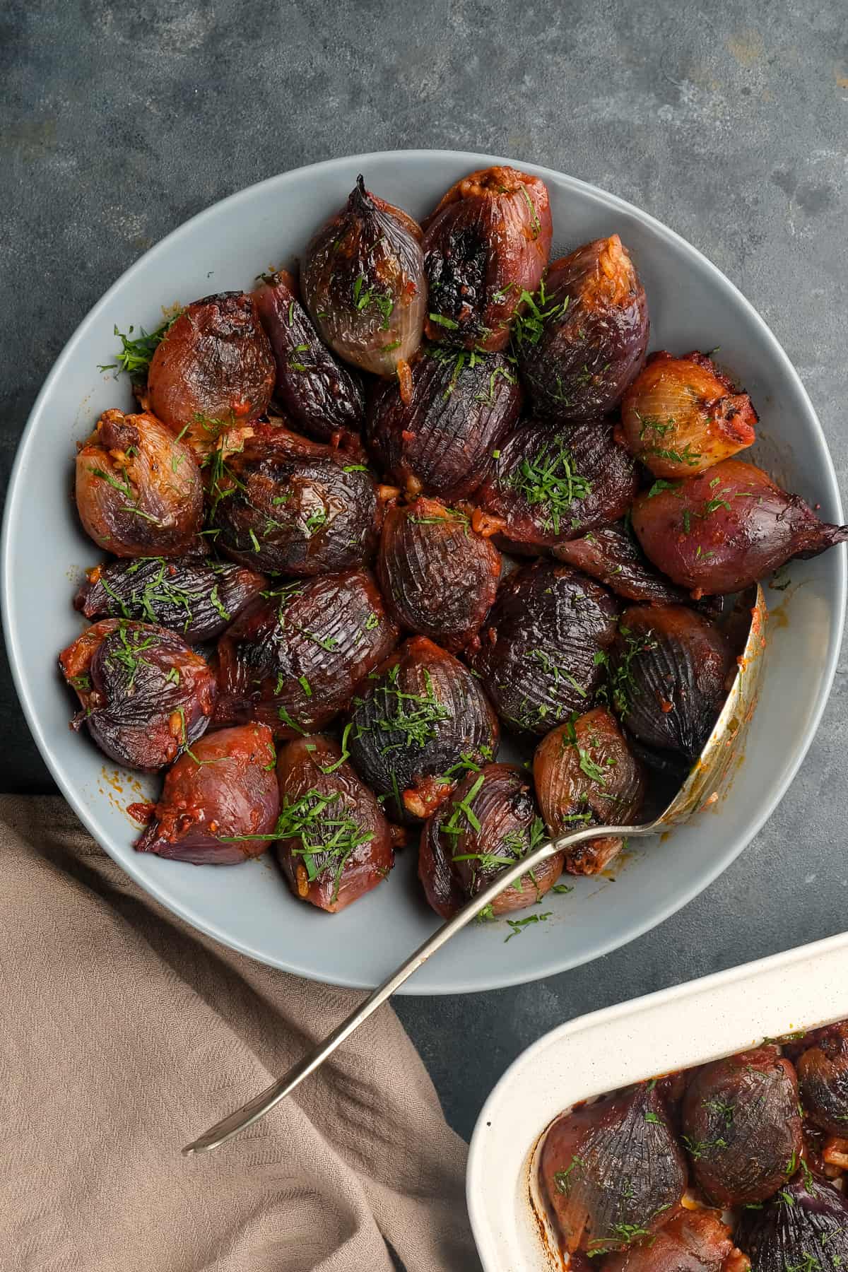 Stuffed purple onions baked in tomato sauce served in a white bowl with a spoon in it.