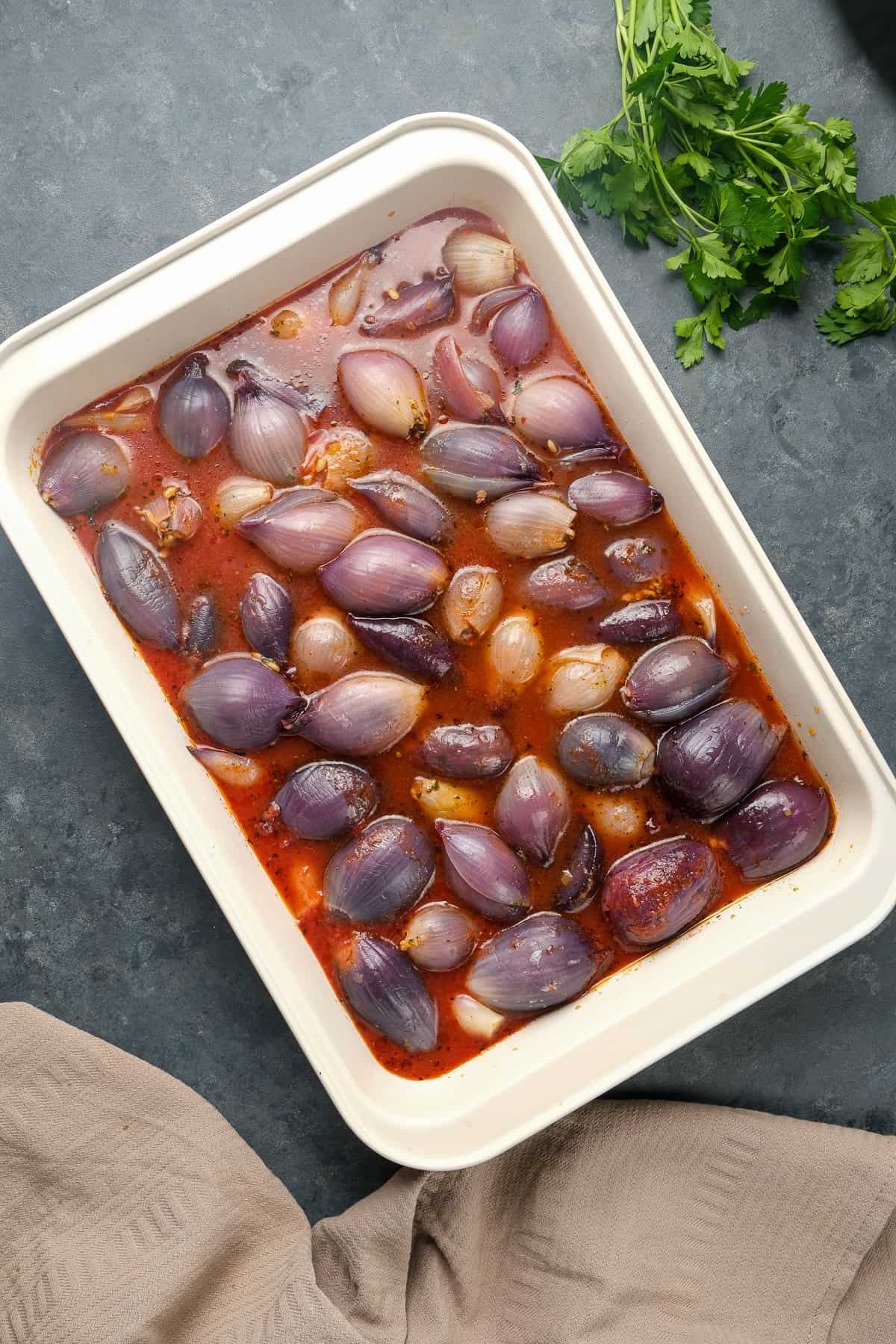 Stuffed onions with a tomato sauce in a baking pan before baked and a bunch of parsley on the side.