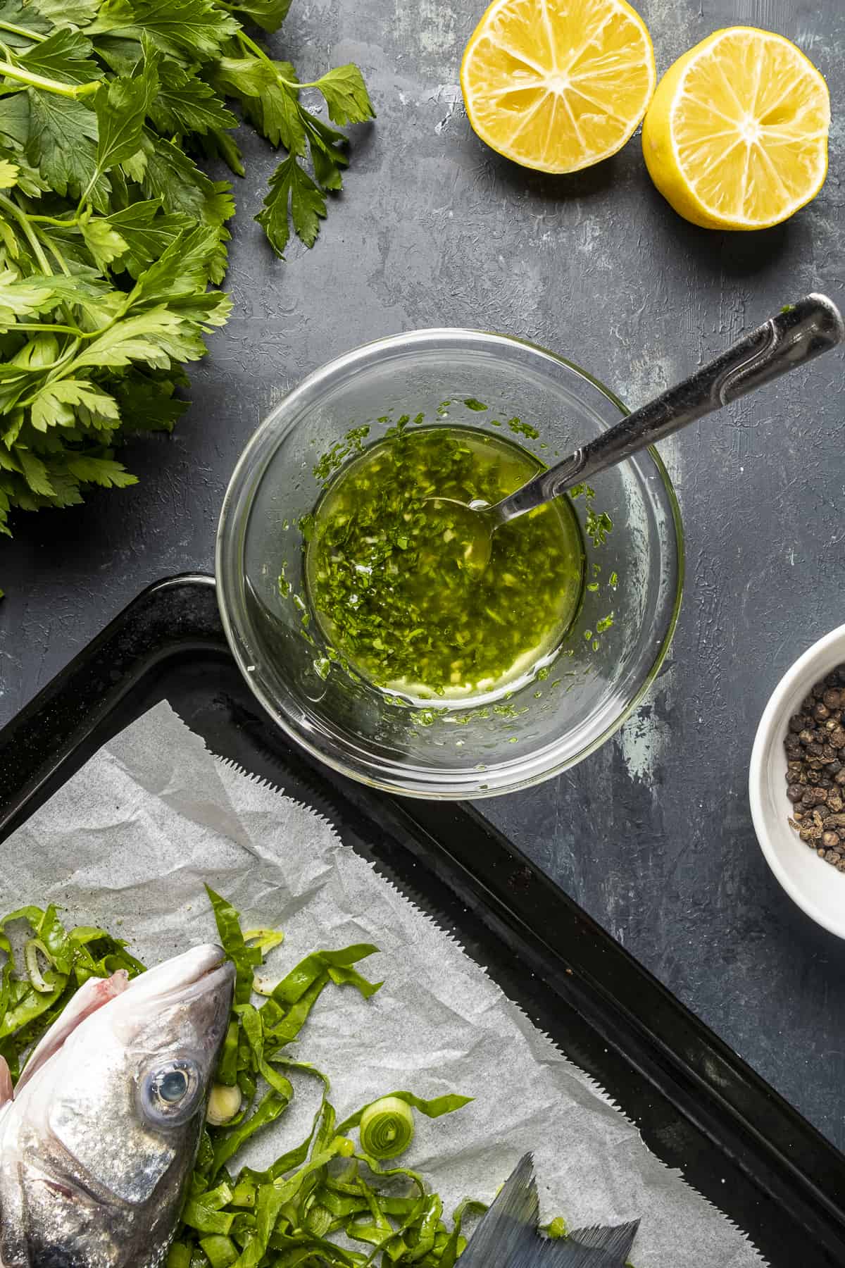 Parsley olive oil sauce in a glass bowl and a spoon in it.