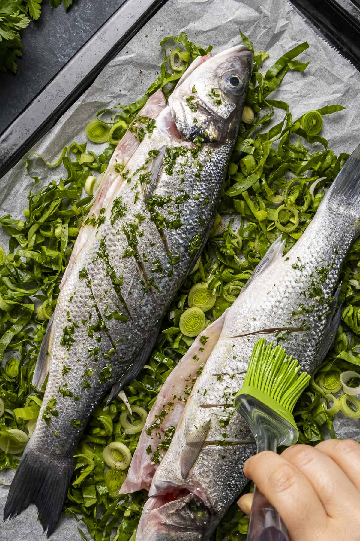 A hand brushing fresh whole fish with a parsley and oil sauce.