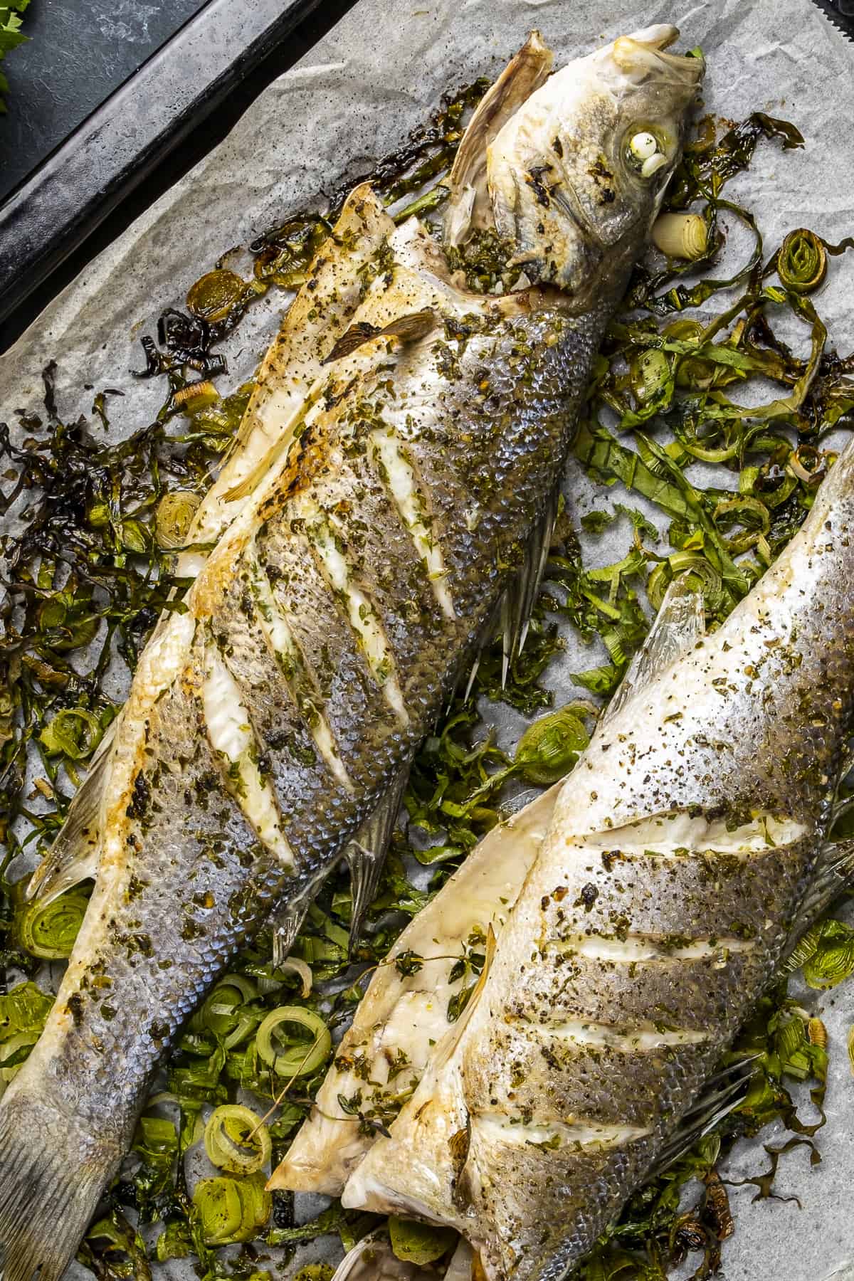 Two baked whole fish on roasted green vegetables in a baking pan.